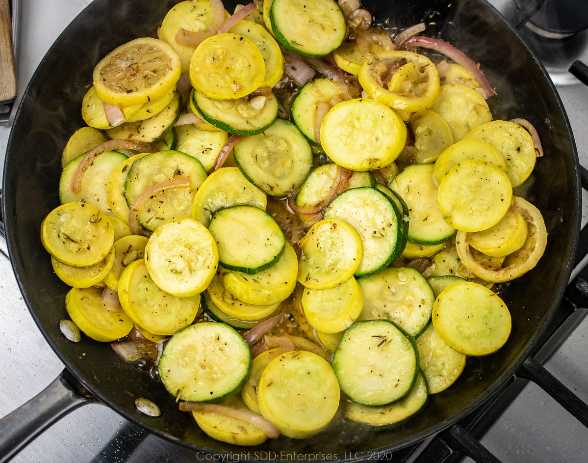 sliced squash and zucchini with onions and spices sauteing in a pan