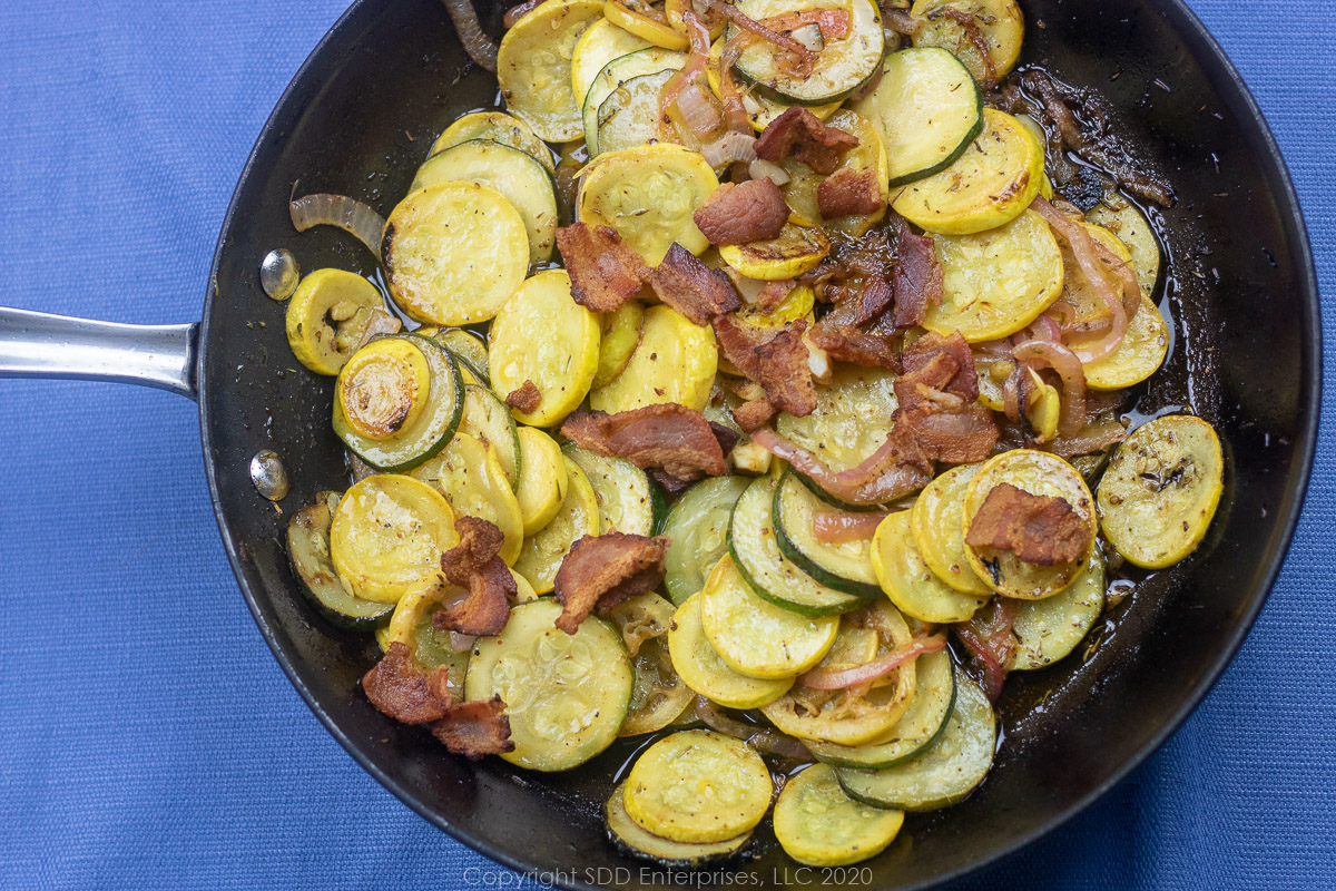 sautéed yellow squash and zucchini with bacon pieces in a skillet.