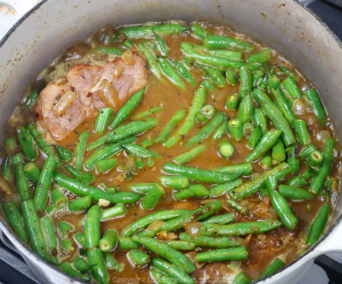 green beans and ham simmering in stock in a dutch oven