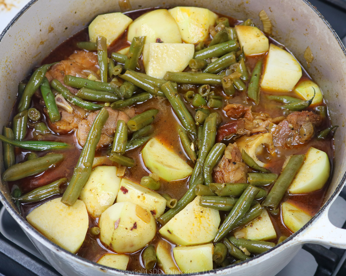 potatoes added to green beans and ham in a dutch oven