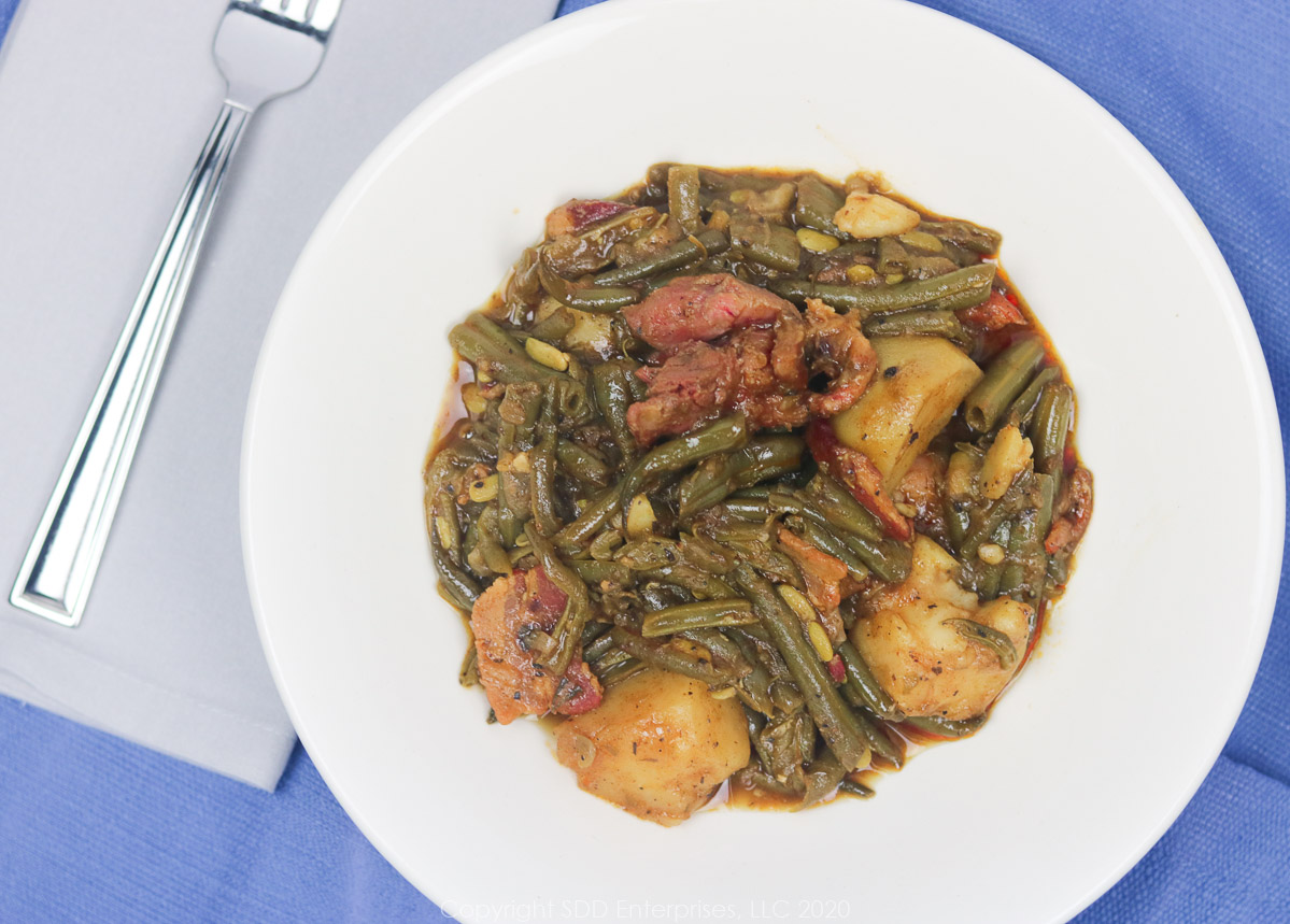 smothered green beans with potatoes in a white bowl with napkin and fork