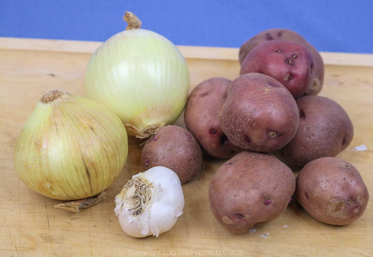 red potatoes, yellow onions and garlic pods on a cutting board