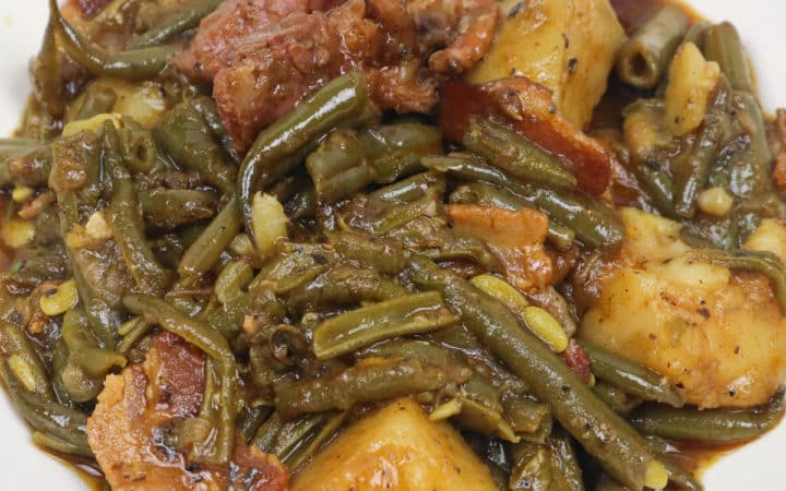 green beans smothered with potatoes, ham and bacon in a white bowl