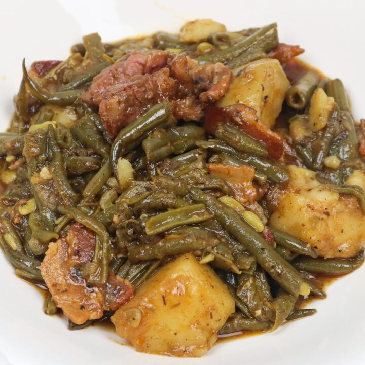 green beans smothered with potatoes, ham and bacon in a white bowl