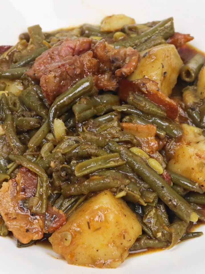 green beans smothered with potatoes, ham and bacon in a white bowl