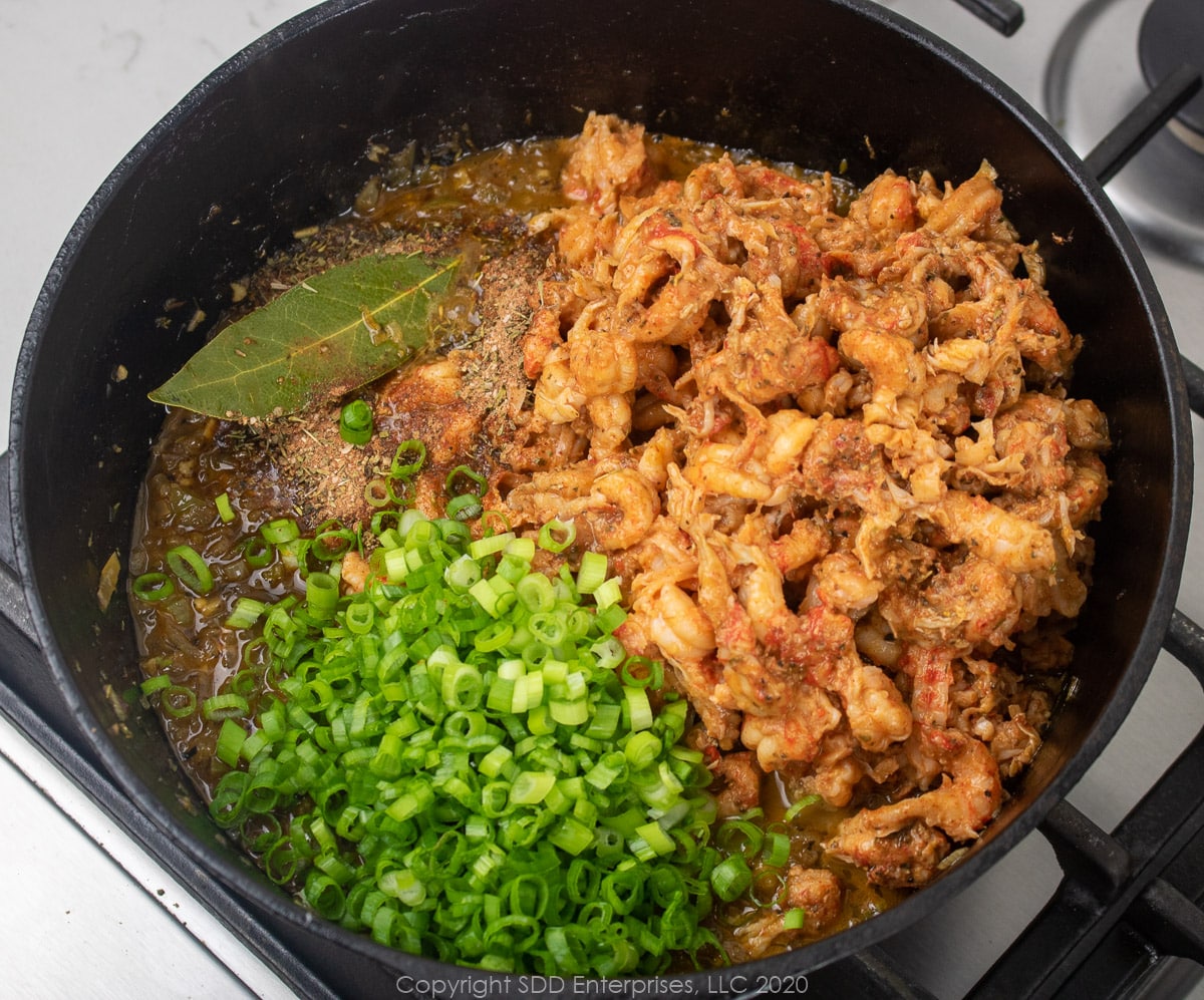 crawfish tails and green onions added to vegetables in a dutch oven for stuffed peppers