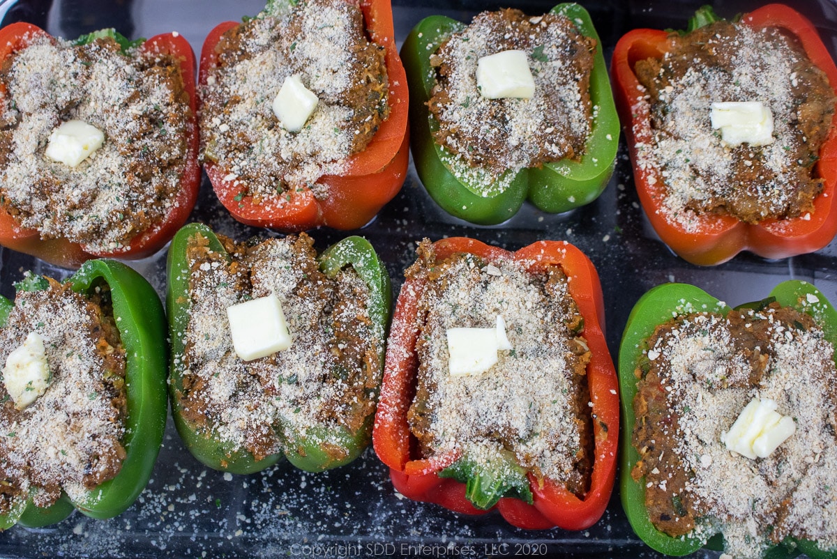 stuffed bell peppers with breadcrumbs and butter on top in a baking dish ready for the oven