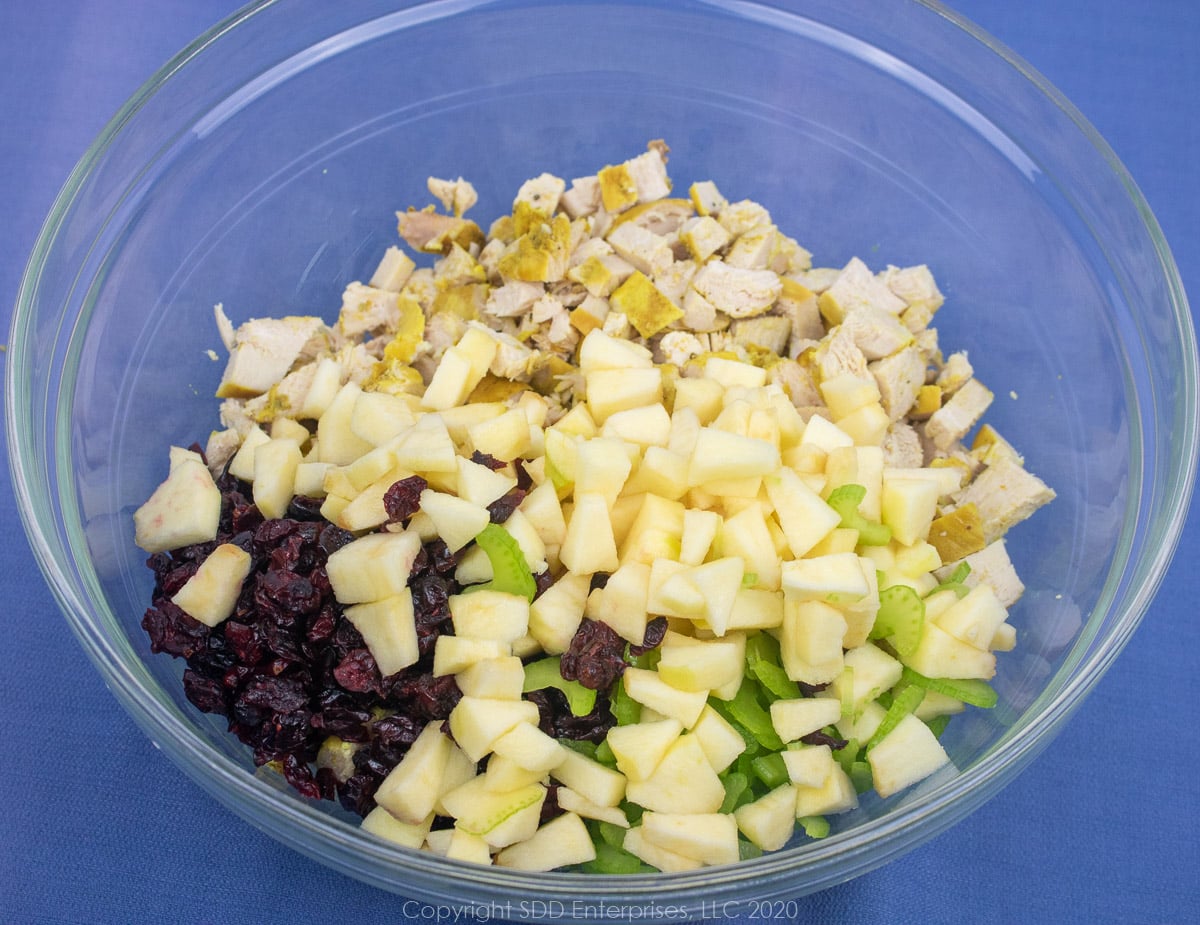 chopped apples and clery and dried cranberries with diced chicken in a clear bowl
