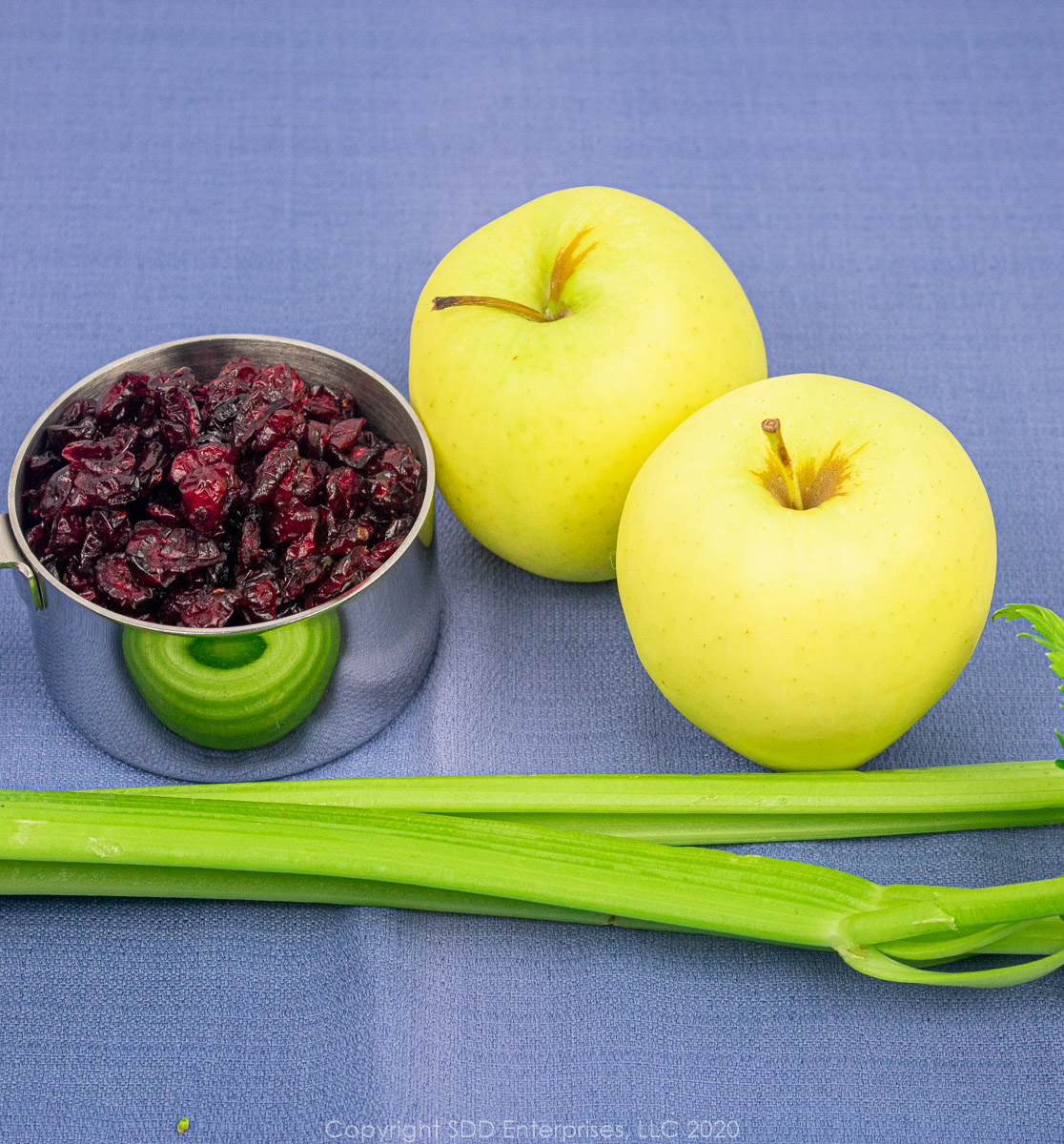 celery, two golden delicious apples and dried cranberries in a measuring cup
