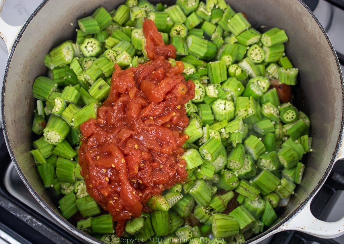 sliced okra and tomatoes in a dutch oven with onions and tasso
