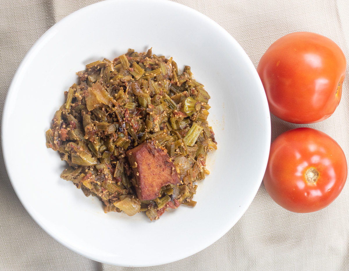 stewed okra with ham and tomatoes in a white bowl with two fresh tomatoes