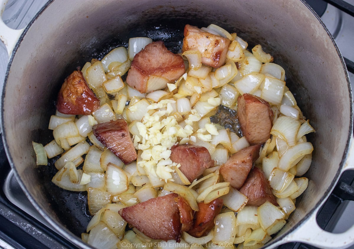 onions and garlic with tasso frying in bacon grease in a dutch oven