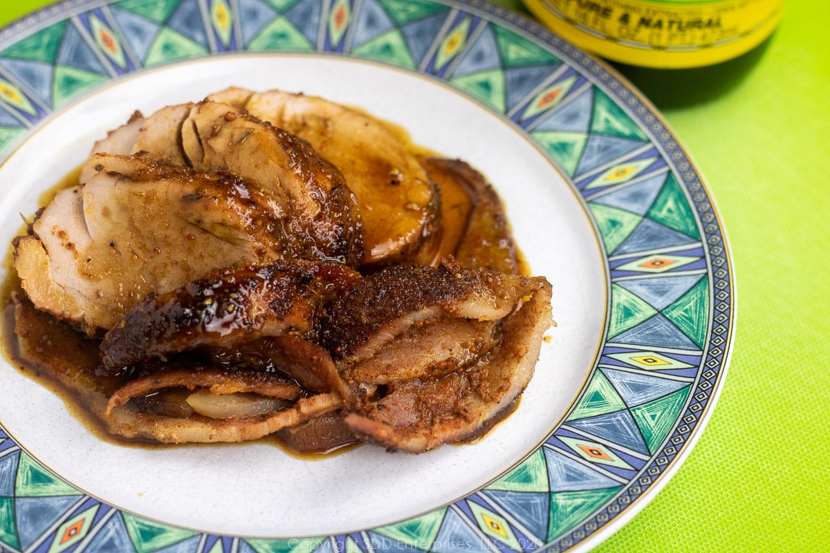 sliced pork tenderloin and bacon with cane syrup sauce on a white plate with green-blue trim