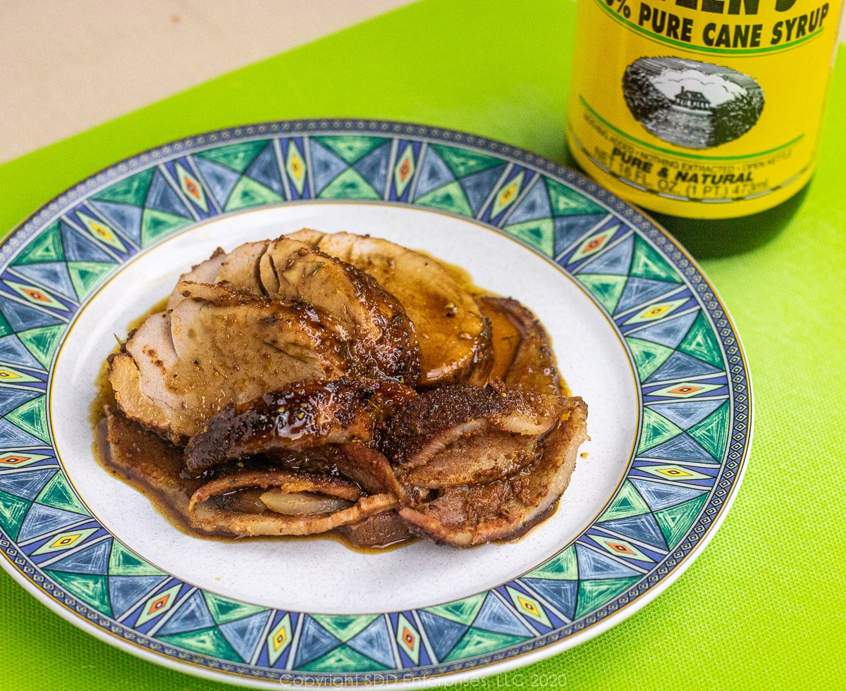 sliced pork tenderloin with bacon and cane syrup sauce on a plate with cane syrup bottle