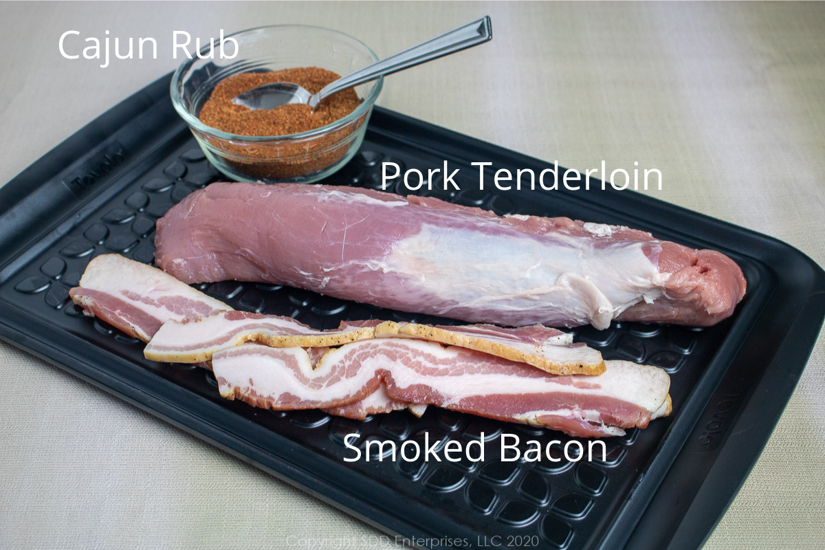pork tenderloin, cajun rub and smoked bacon on a prep board with graphics