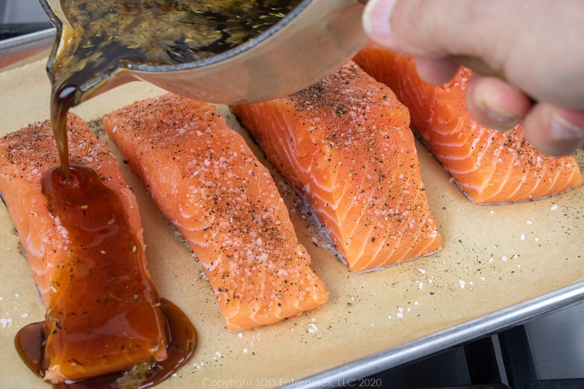 cane syrup sauce being poured over salmon filets on a baking sheet