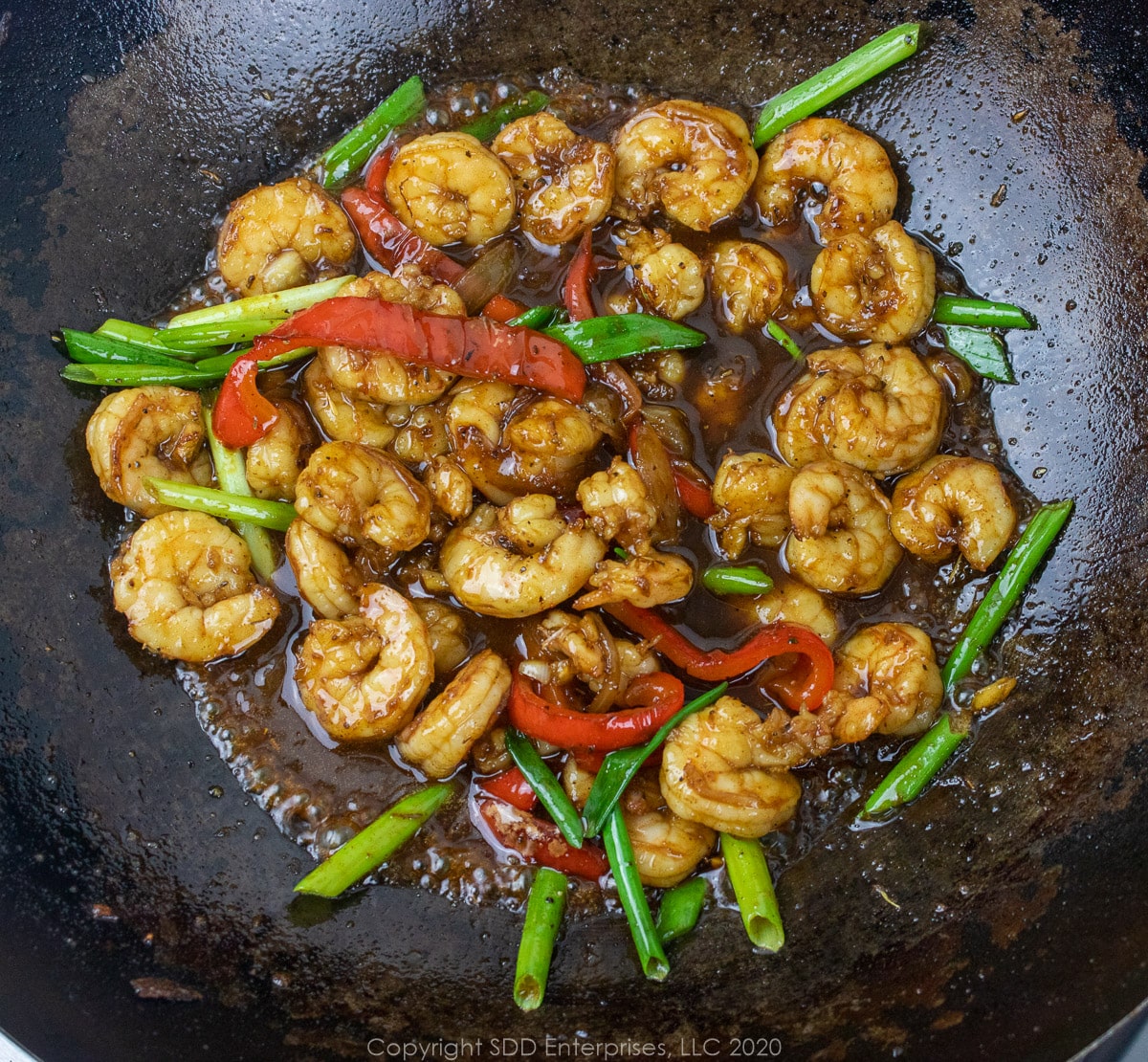 cane syrup sauce in the shrimp and onions and peppers in a wok