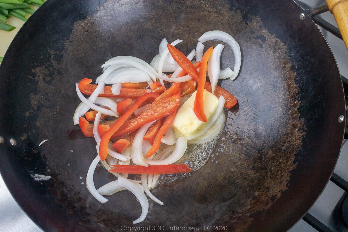 onions and peppers sauteeing in butter in a wok