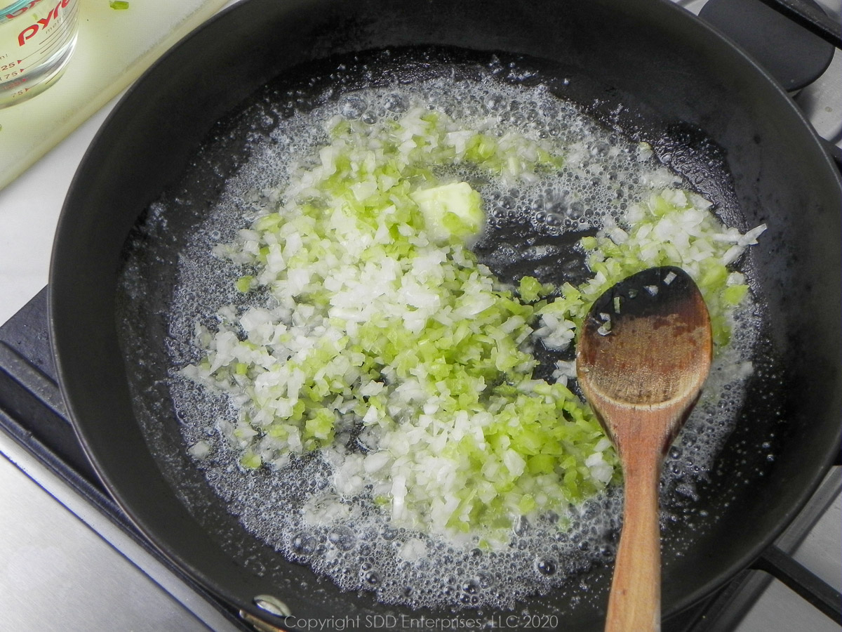 yellow onions and celery sauteing in butter in a frying pan