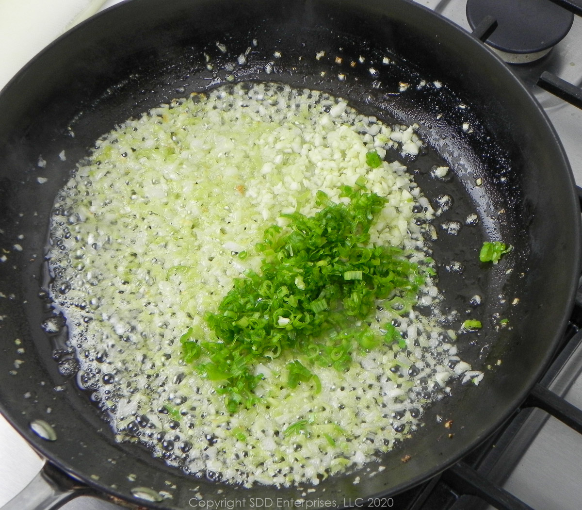 green onions and garlic with yellow onions and celery in butter in a frying pan