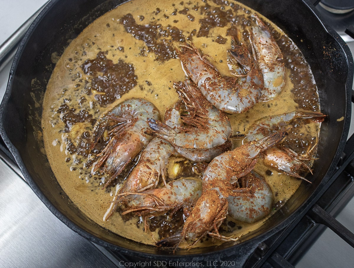 large shrimp added to sauce in a cast iron skillet for barbecued shrimp