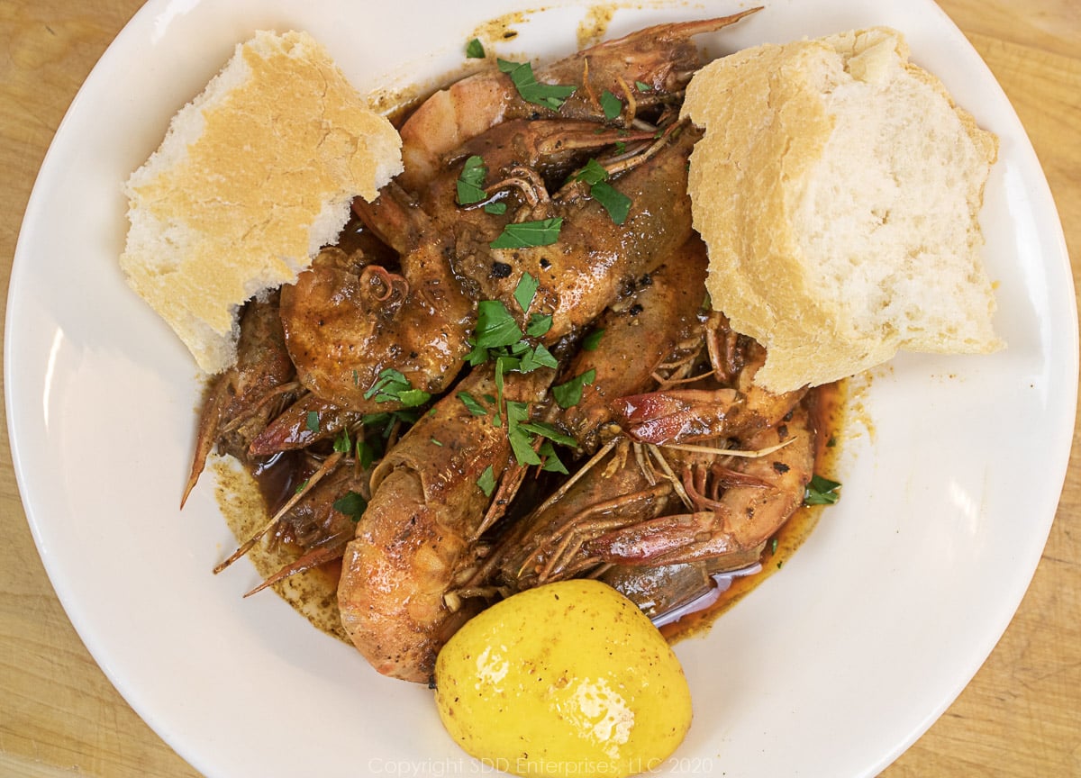 barbecued shrimp in a white bowls with lemon wedges and french bread