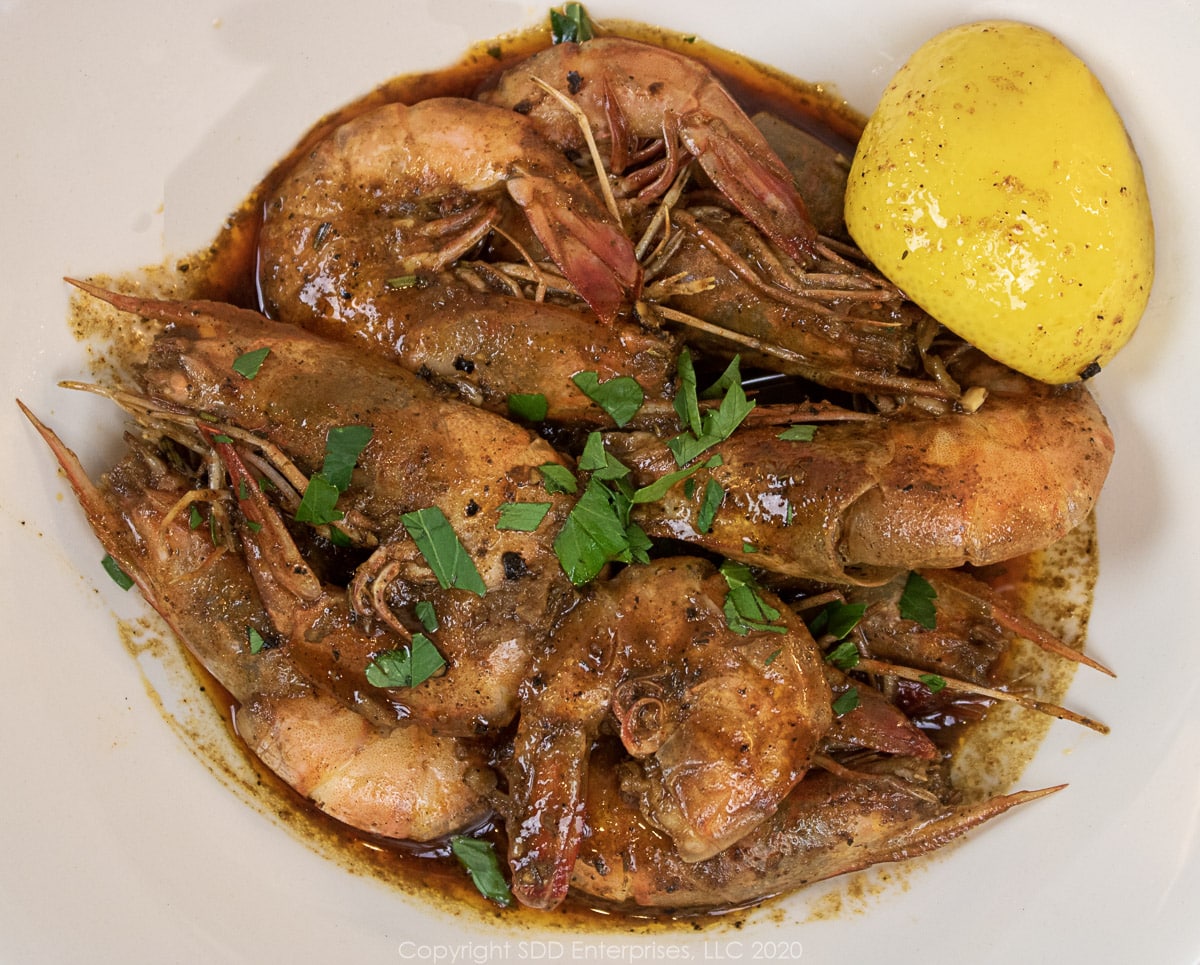 barbecued shrimp in a white bowl sprinkled with parsley and a lemon wedge 