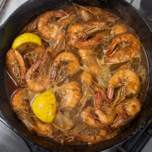 bbq shrimp in a cast iron skillet with lemon wedges