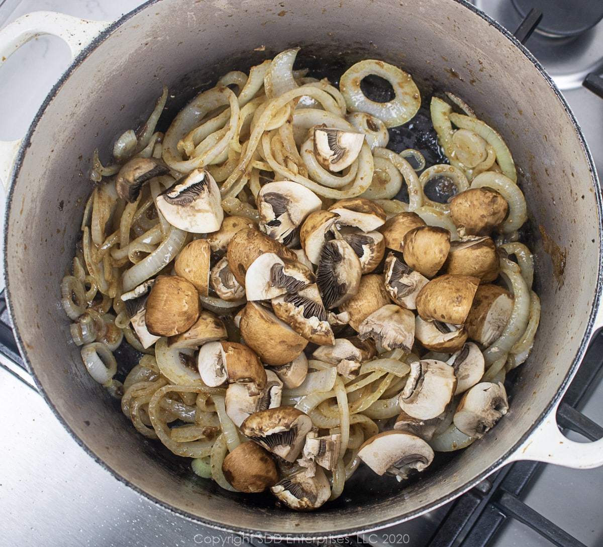 mushrooms and yellow onions frying in a dutch oven