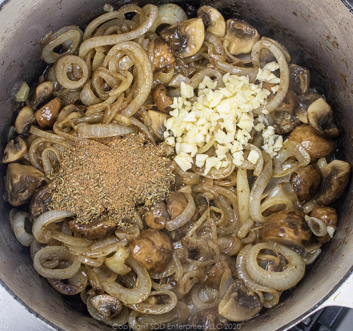spices and garlic with mushrooms and yellow onions cooking in a dutch oven