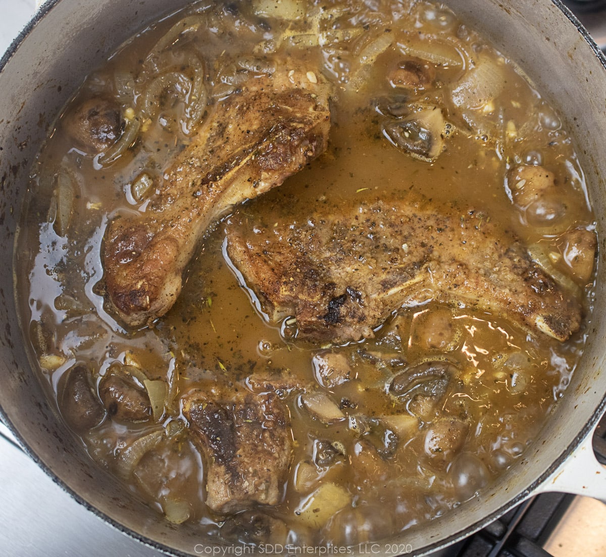 seared pork chops added to stock and vegetables in a dutch oven