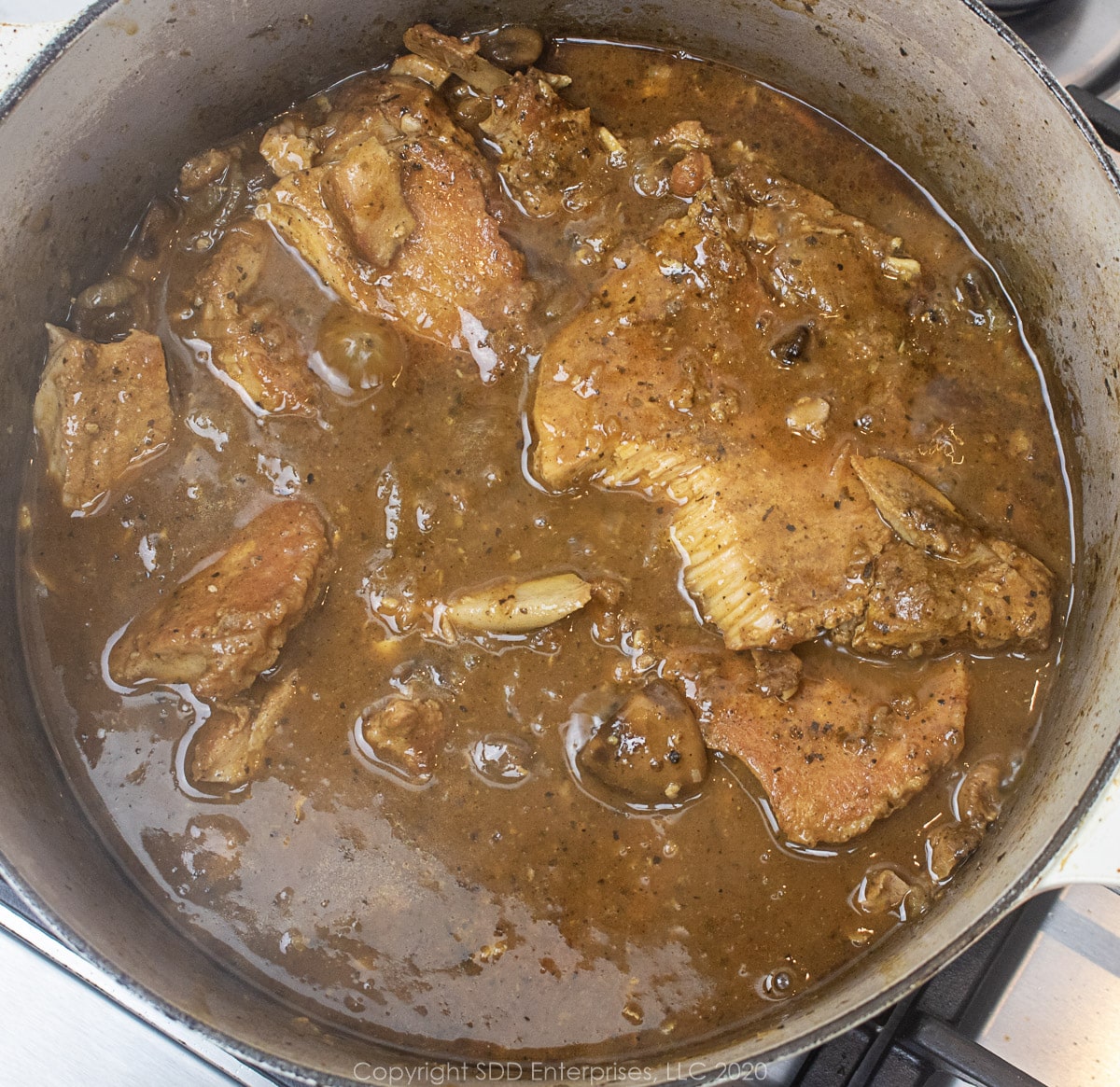 smothered pork chops simmering in gravy in a dutch oven