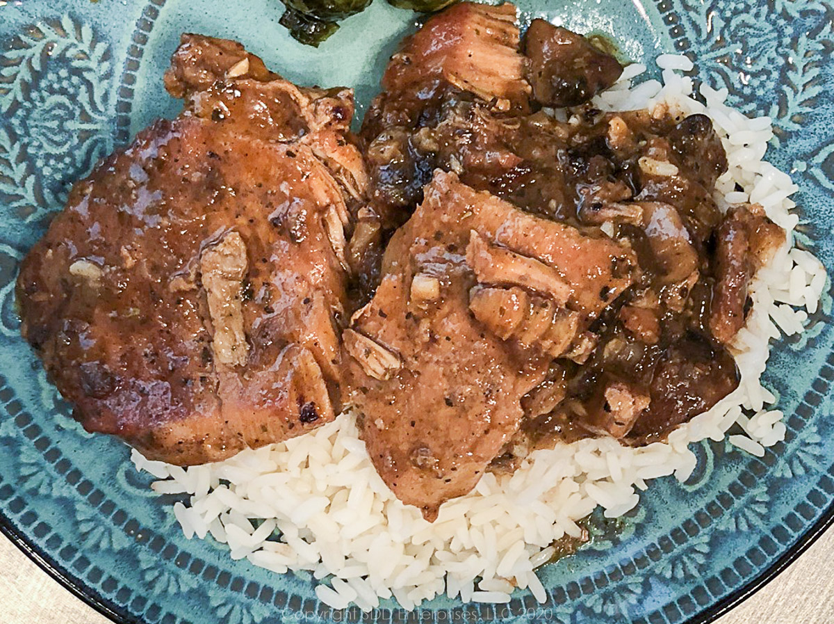 smothered pork chops served over rice on a lue-green plate