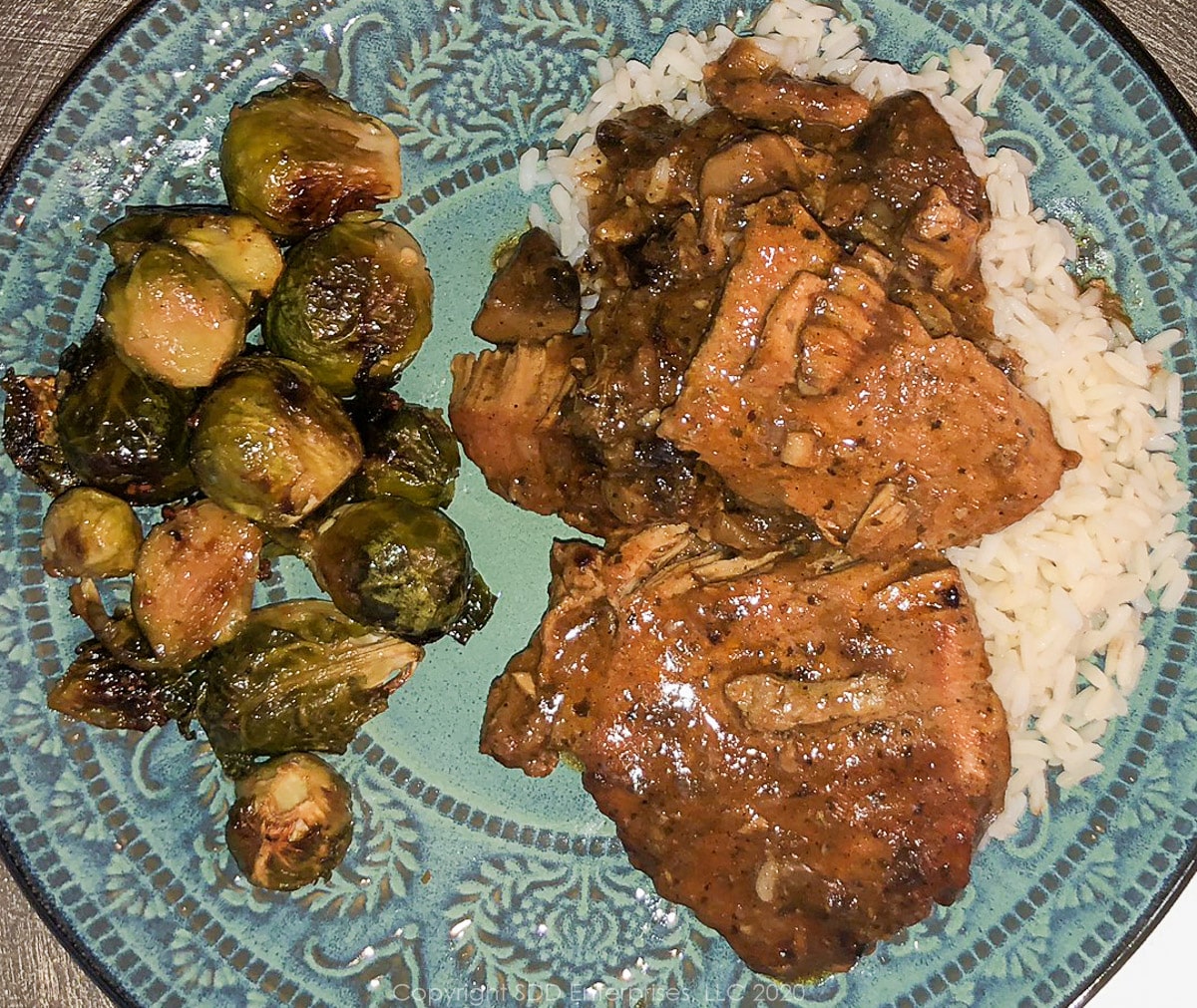 smothered pork chops with roasted brussels sprouts on a blue-green plate