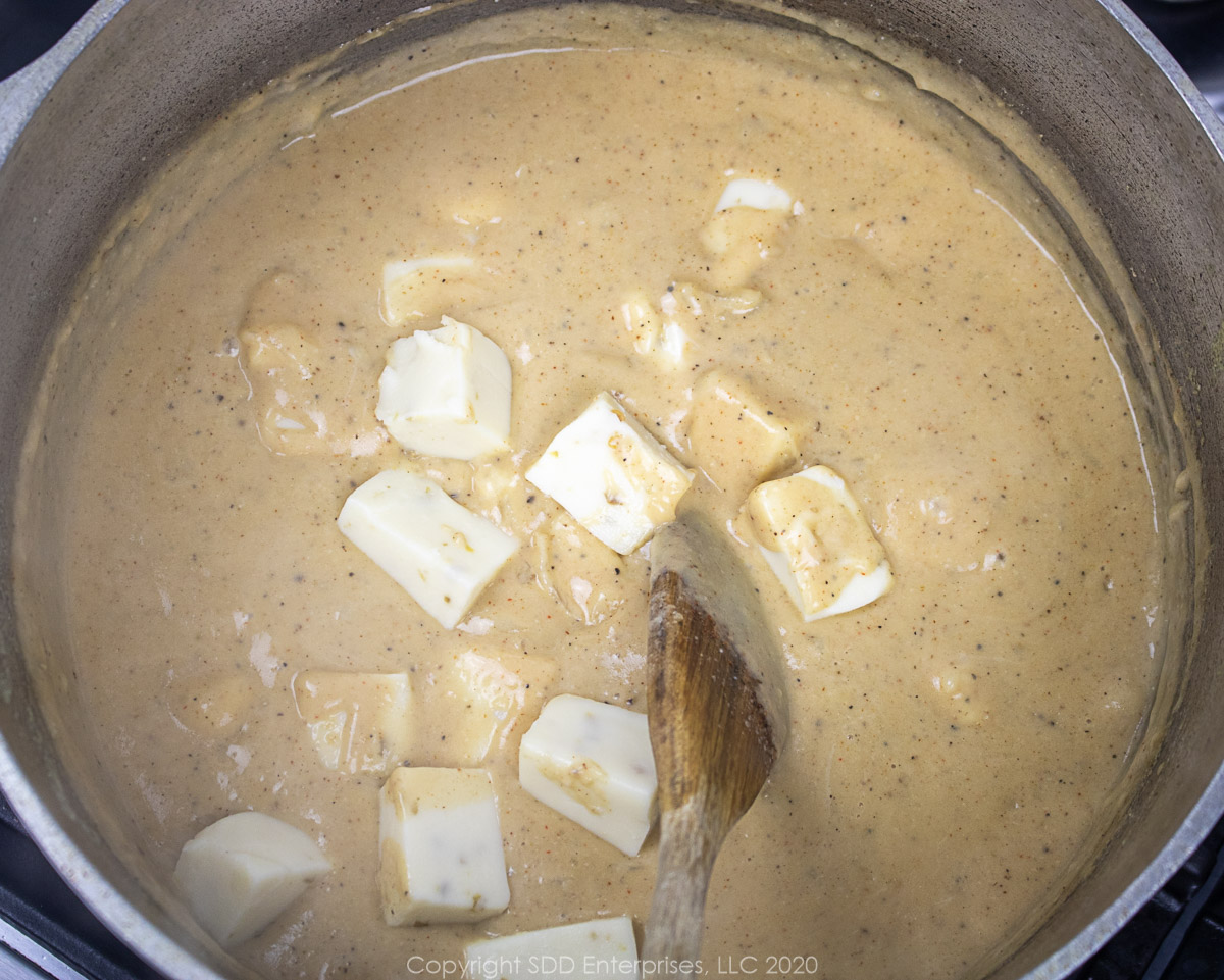 cubed cheese added to cream sauce in a dutch oven