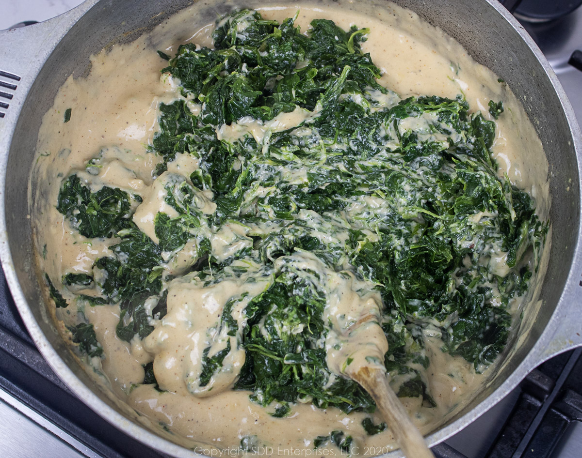 spinach blended into cheese sauce in a dutch oven