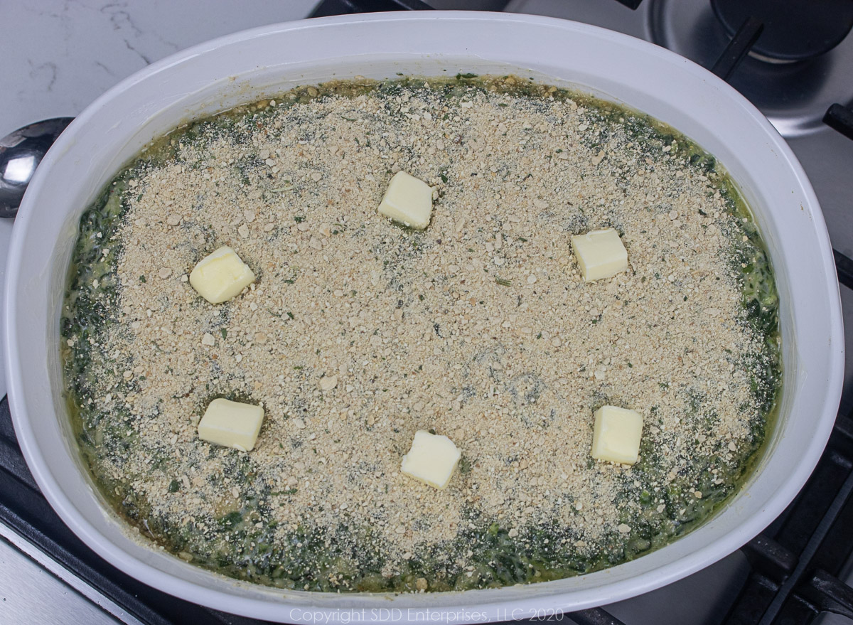 spinach Madeline in a white casserole dish with breadcrumbs and butter on top ready for the oven