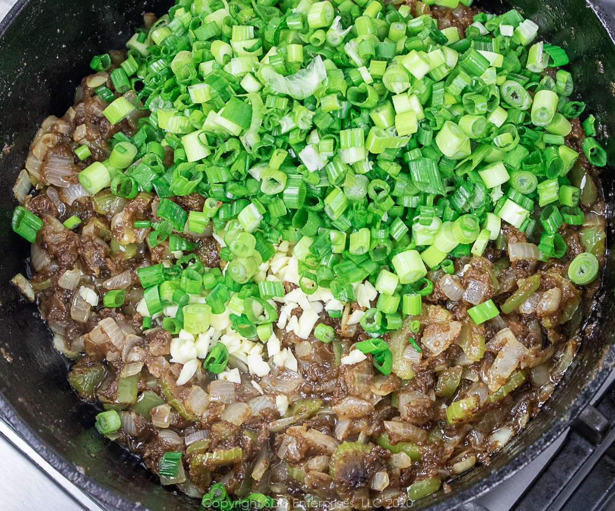 green onions and garlic added to a roux and onions in a dutch oven