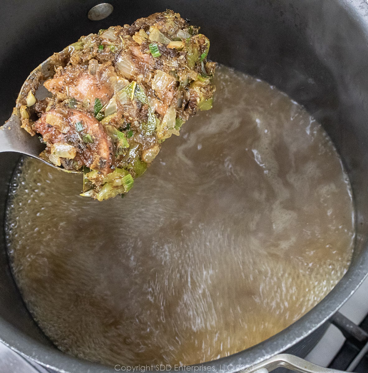 a spoonful of roux/veggie mix being added to a stock in a stockpot