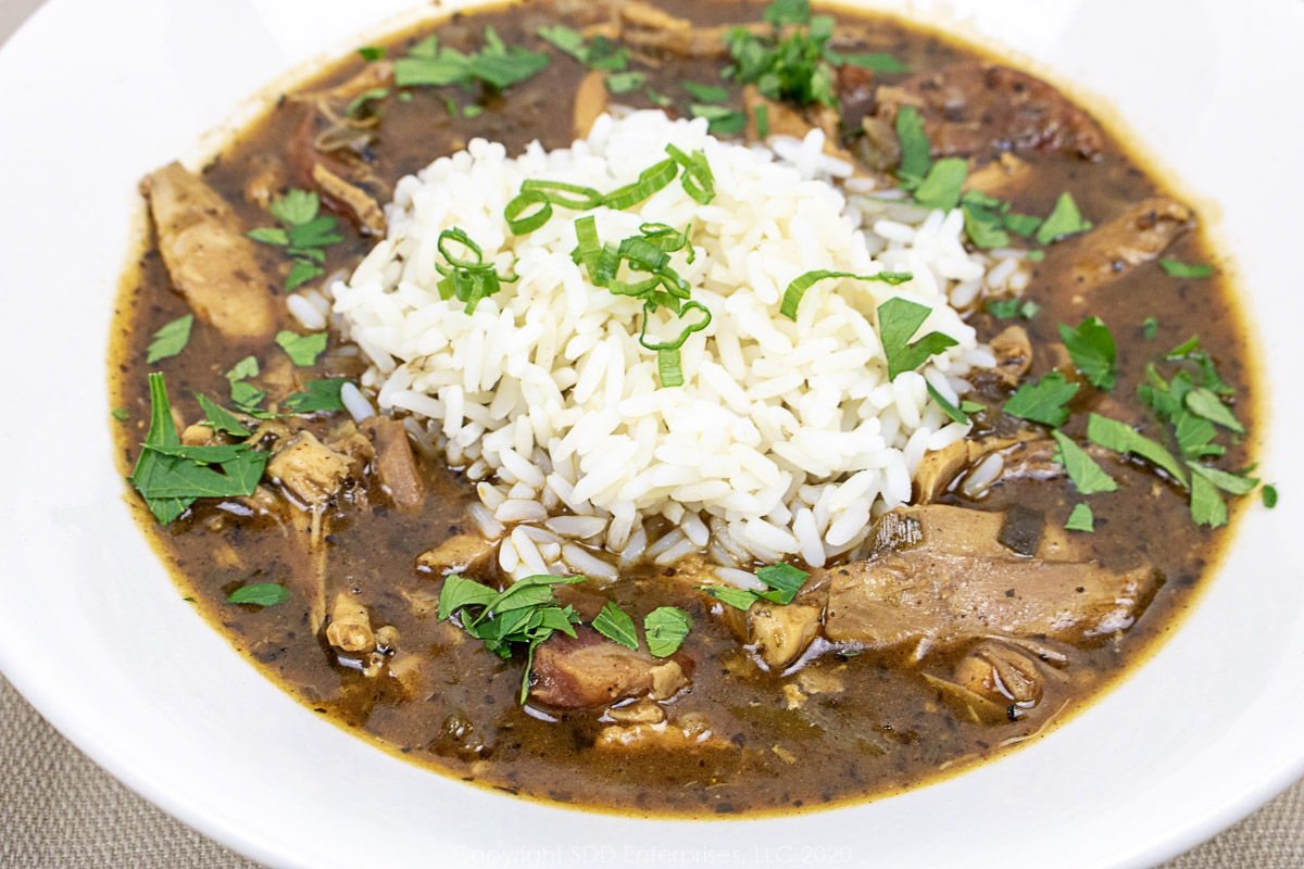 chicken and andouille gumbo with rice and garnish in a white bowl
