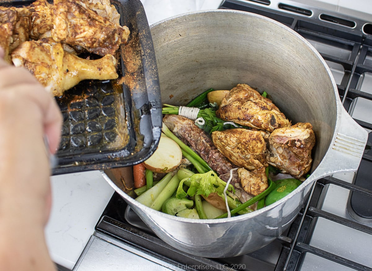 chicken being added to a stockpot with vegetables in a stockpot
