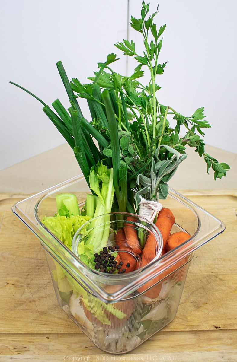 prepared vegetables and seasoning for chicken stock in a cambro prep bowl