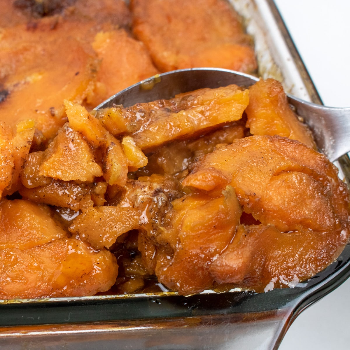 baked candied yams in a baking dish with a serving spoons