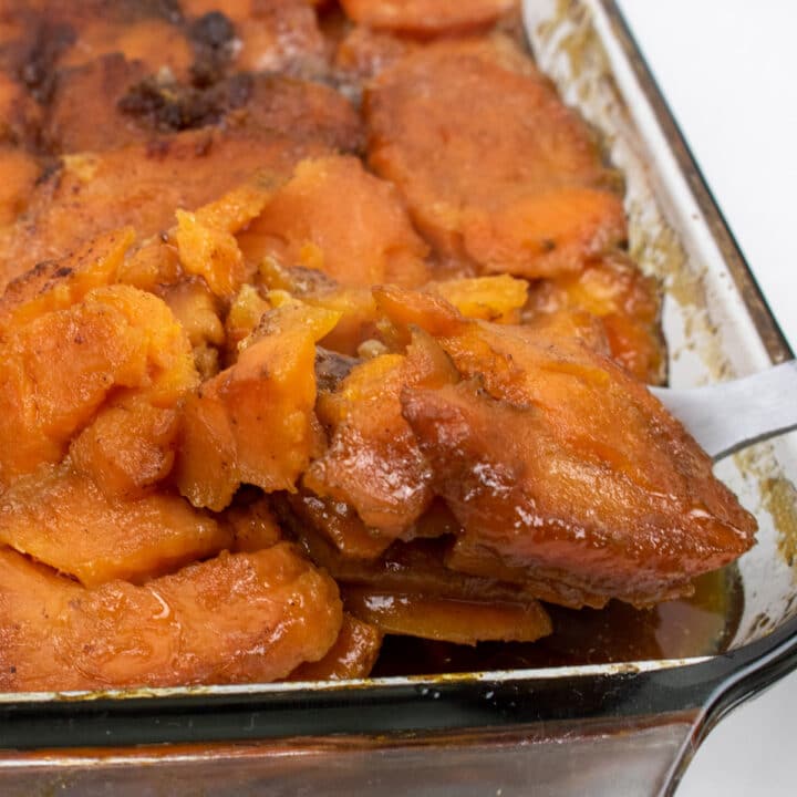 candied yams in a glass baking dish with a serving spoon inserted