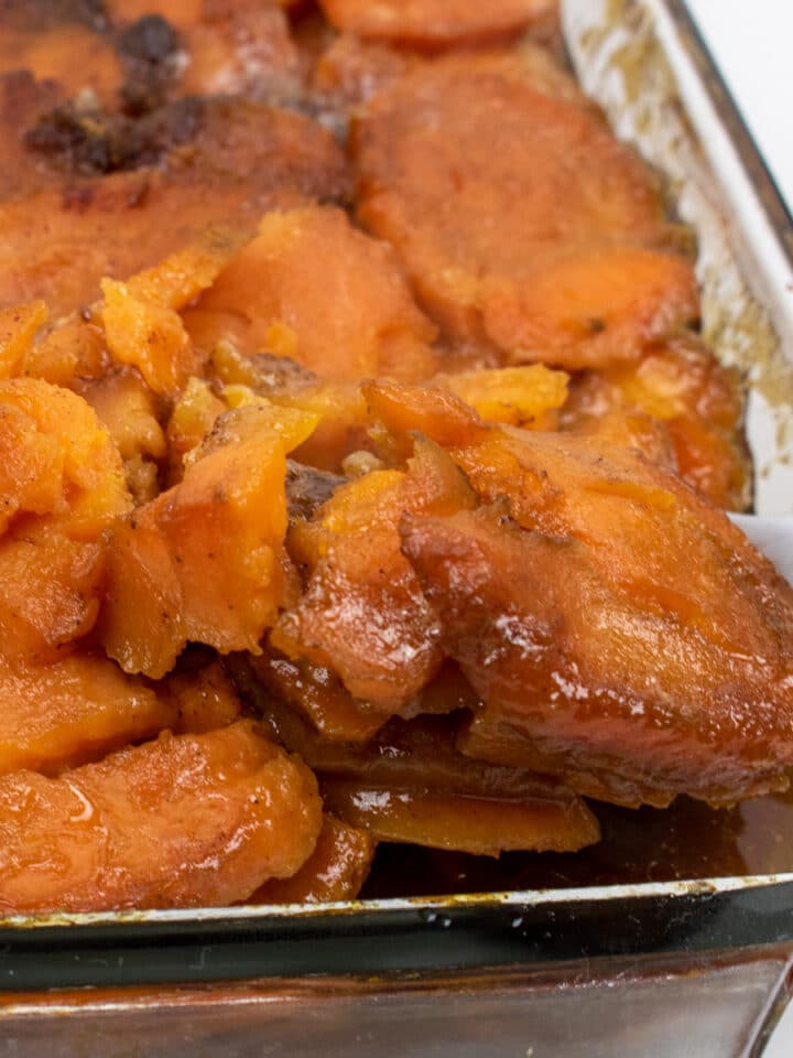 candied yams in a glass baking dish with a serving spoon inserted