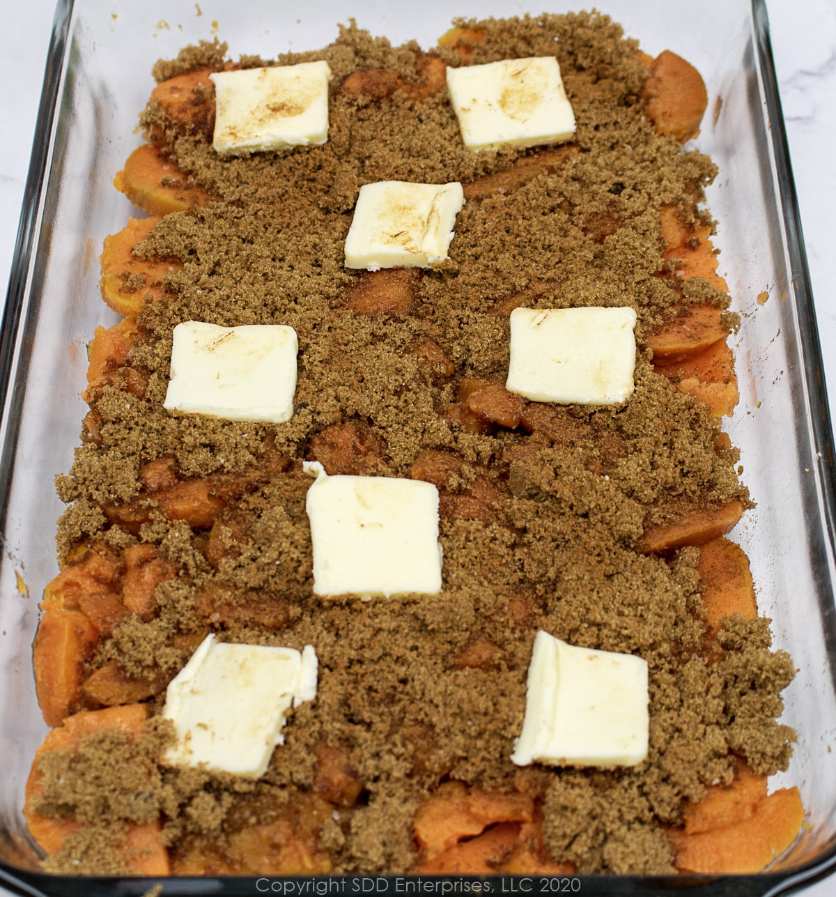 sliced sweet potato layer with brown sugar, cinnamon and butter in a baking dish