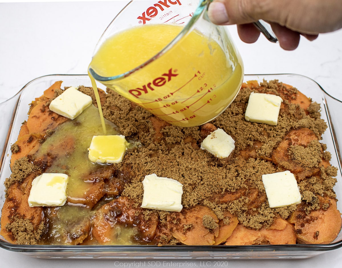 pouring orange juice over prepared candied yams before baking