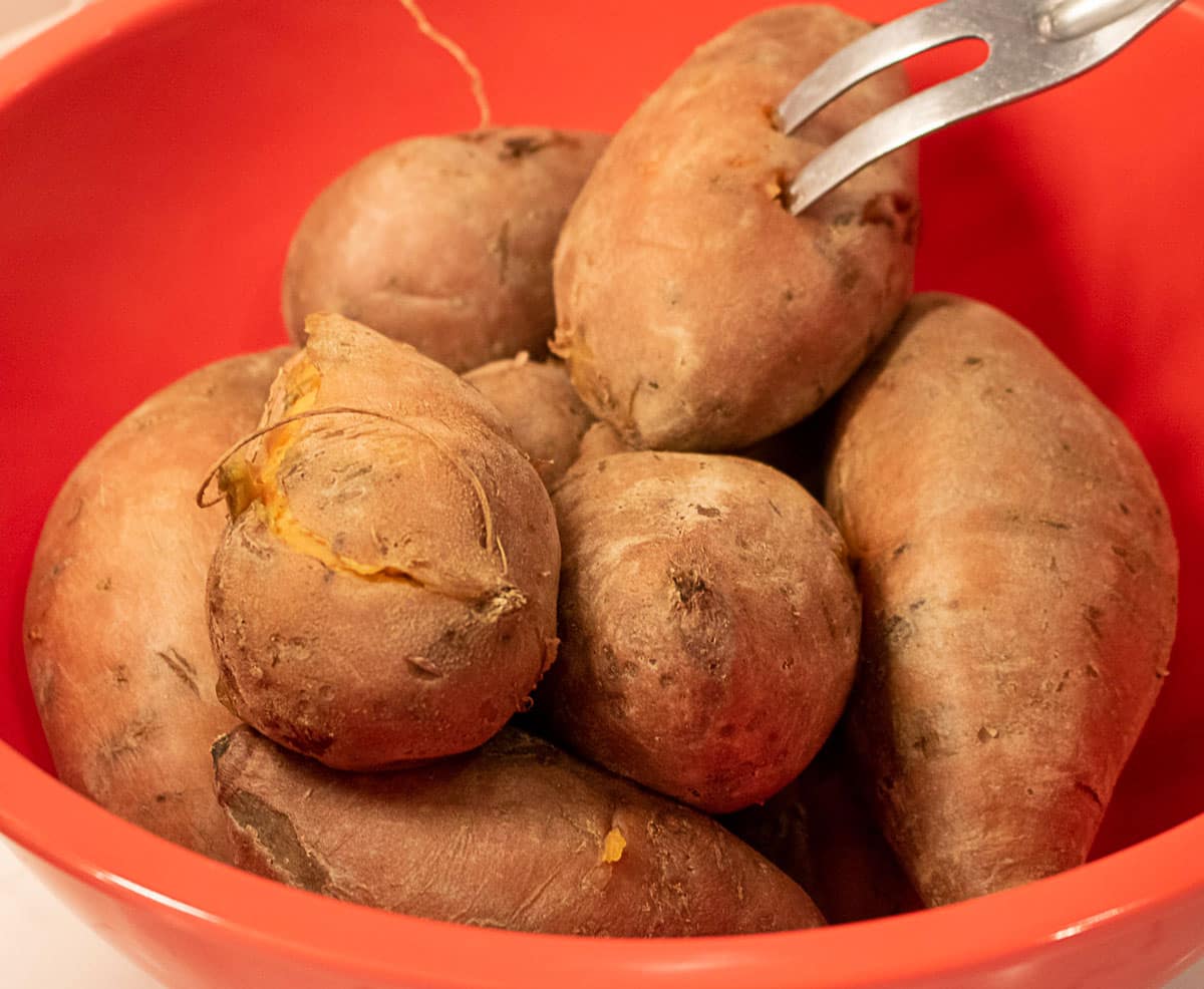 cooked sweet potatoes in a red bowl with a fork probe