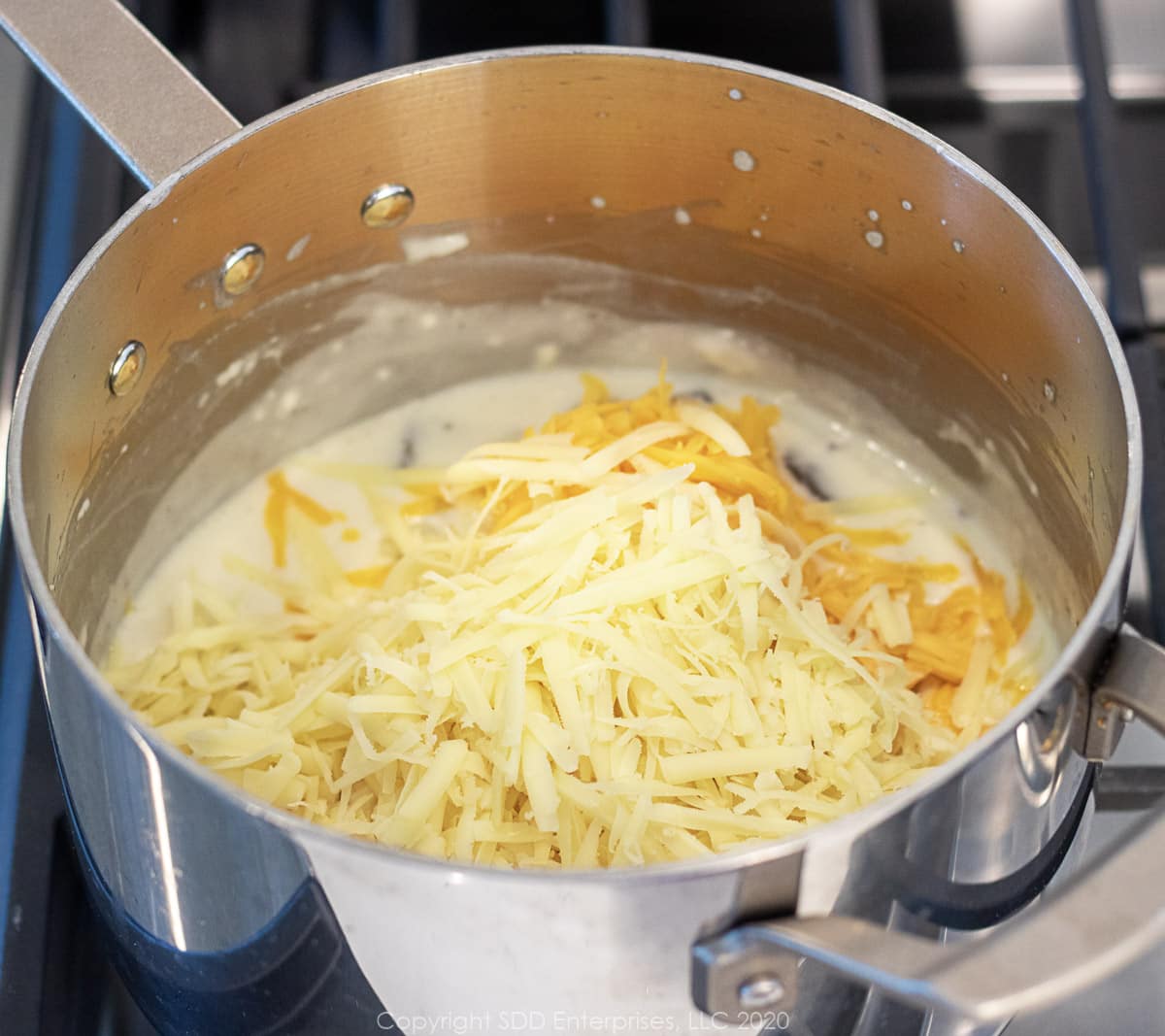 cheddar and gruyere cheeses added to a bechamel sauce in a sauce pan