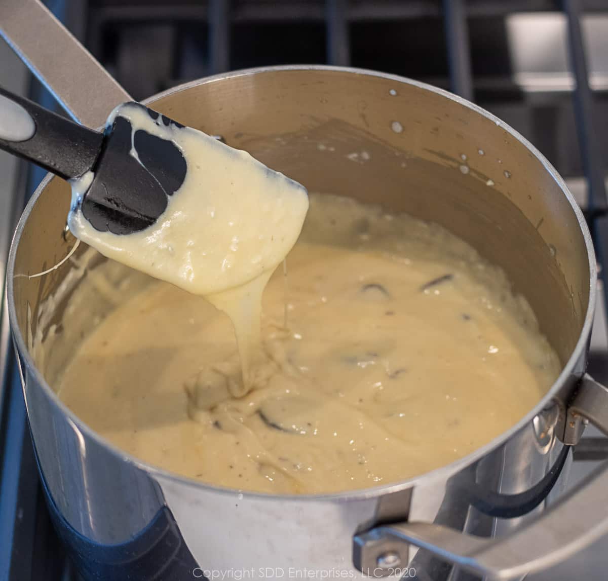 cheesy bechamel sauce in a sauce pan with a spatula